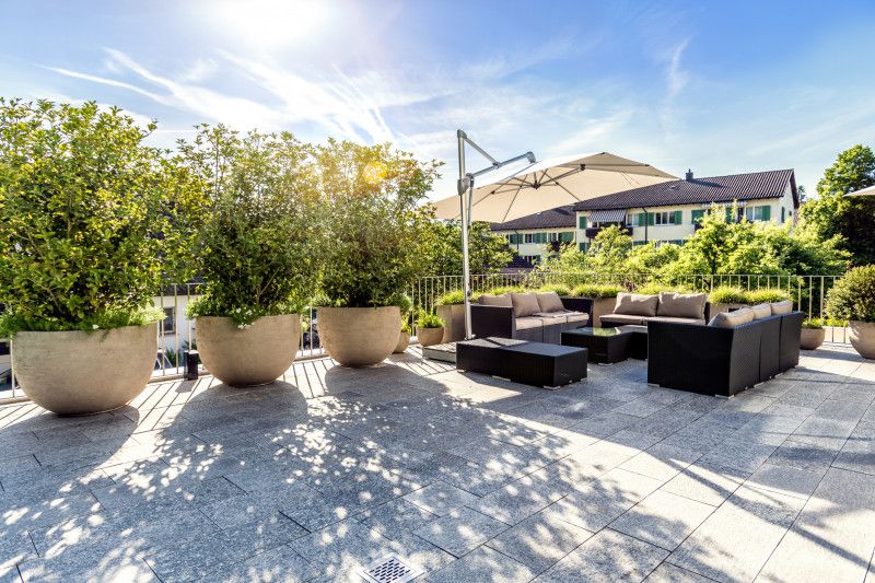 Sonnige Dachterrasse mit Sitzgruppe, Sonnenschirm und grossen Pflanzkübeln auf Flachdach in der Schweiz, Aargau
