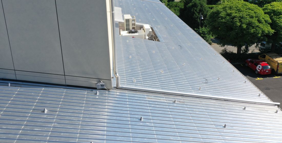 Metalldach mit Blitzschutzinstallationen auf einem Flachdach in Aargau, Schweiz, mit umliegenden Bäumen und Fahrzeugen