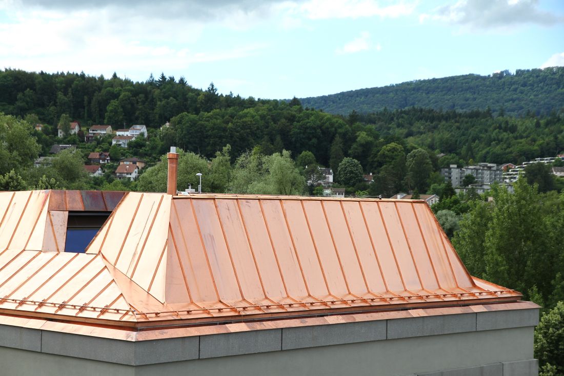Kupfer-Metalldach mit Stehfalztechnik auf Wohnhaus vor bewaldeter Landschaft im Aargau, Schweiz